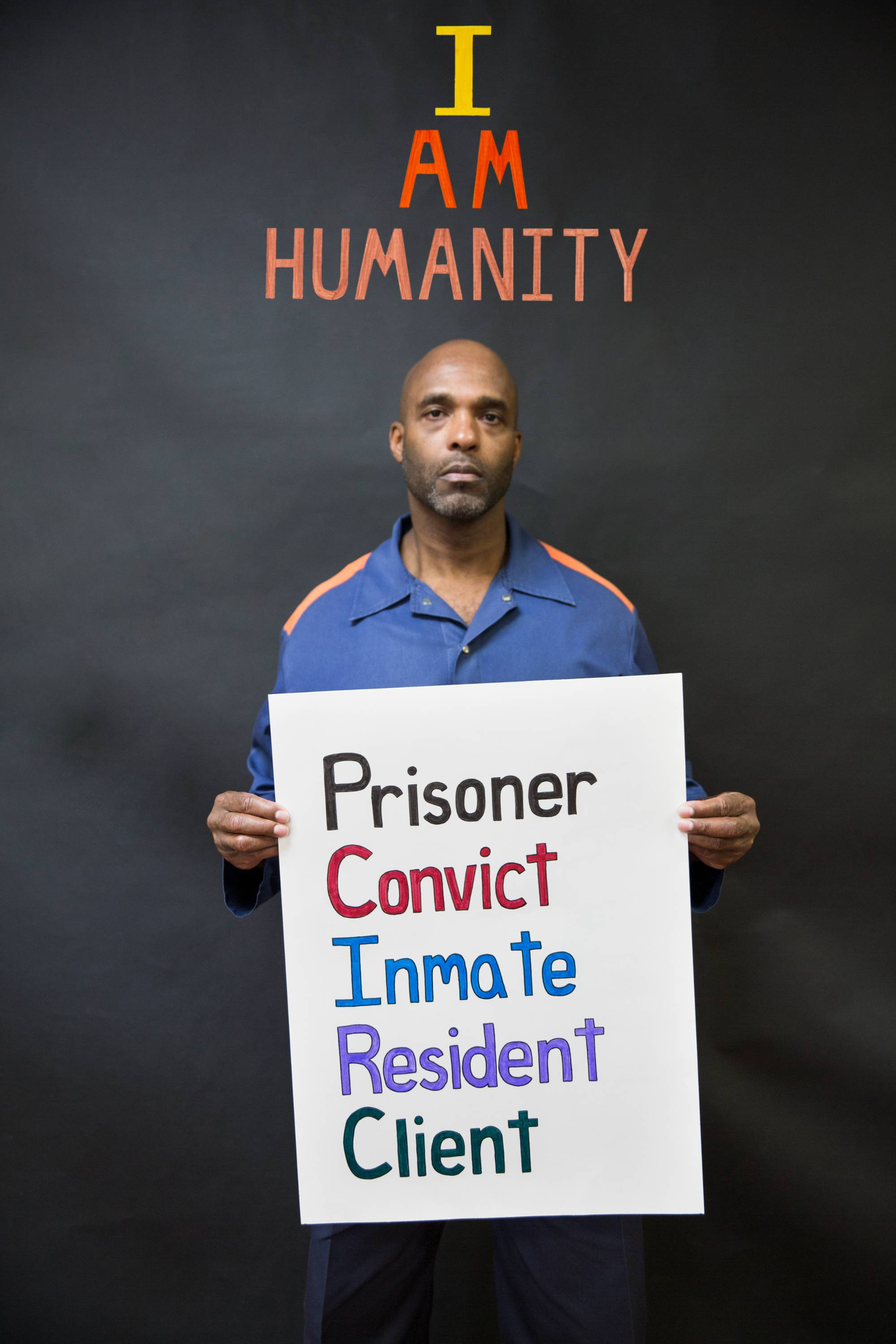 Color photograph of a man holding a sign wearing a blue shirt.